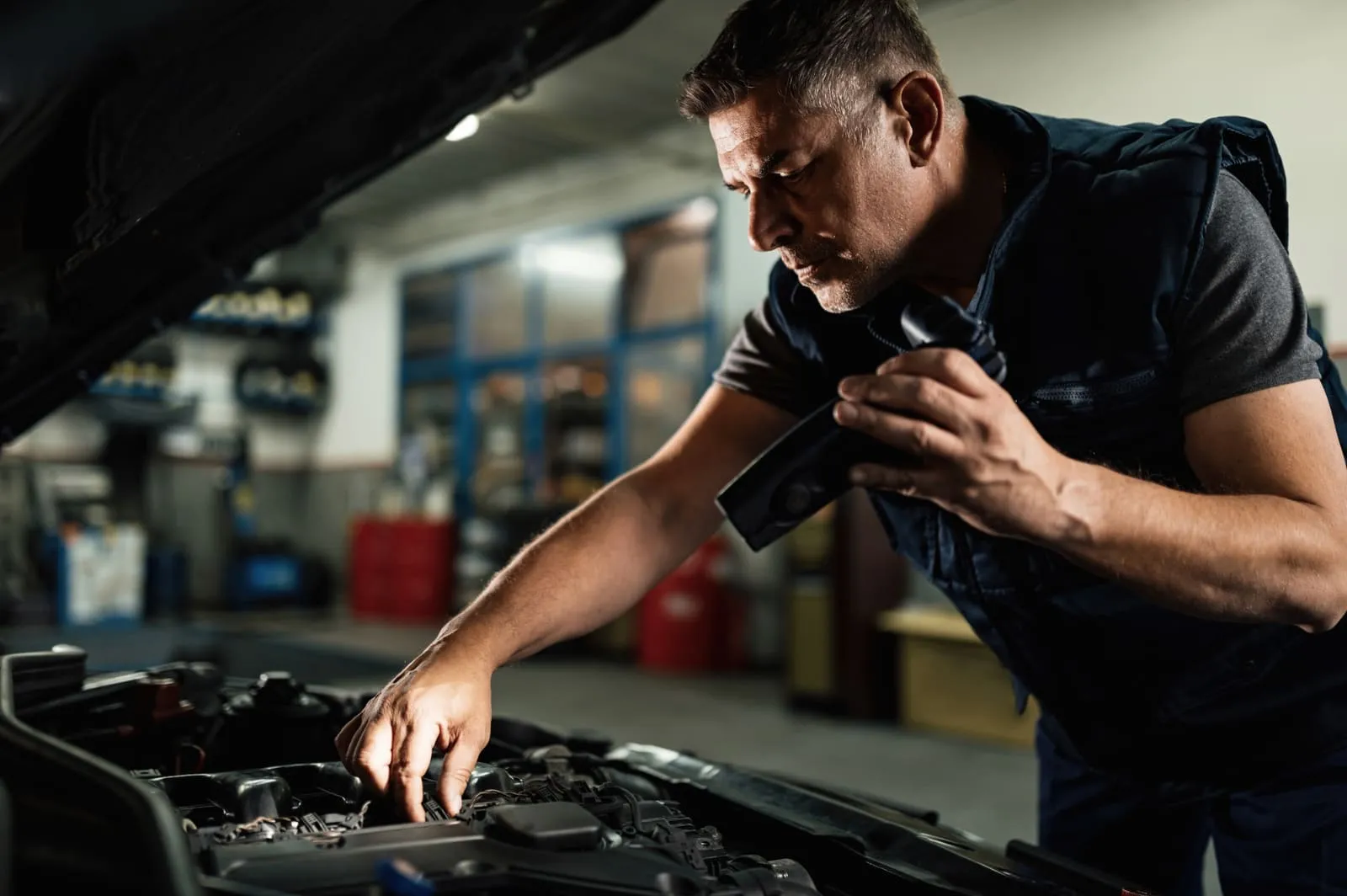 A mechanic inspecting an engine bay with a torch