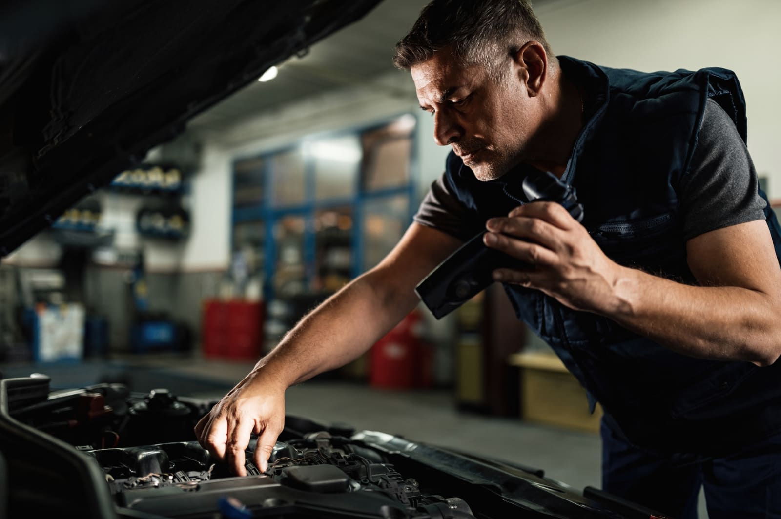 A mechanic inspecting an engine bay with a torch